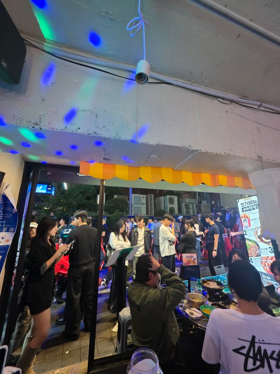입구 안쪽에서 바라본 노란 차양과 길가 자리. 천장에는 미러볼 조명이 돌고 있다