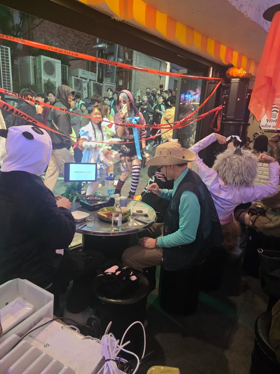 길가 좌석에 앉은 손님들 뒤로 사람들이 오가는 이태원로27가길의 밤. 노란 차양이 보도 위로 뻗어 있다